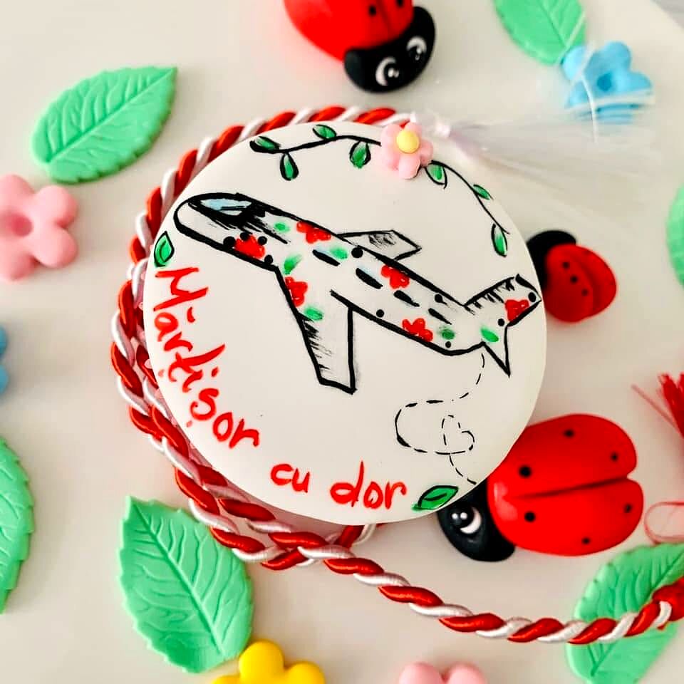 Biscuit-mărțișor pictat cu un avion și șnur roșu-alb